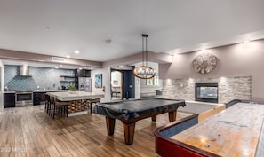 A spacious living area with a pool table, a kitchen with modern appliances, and a stone fireplace.