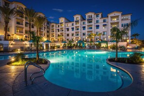 Un hôtel doté d’une piscine entourée de palmiers et de chaises longues.