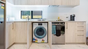 Une cuisine compacte équipée d’un lave-linge et d’un sèche-linge intégrés, d’une machine à café et d’une fenêtre donnant sur l’extérieur.