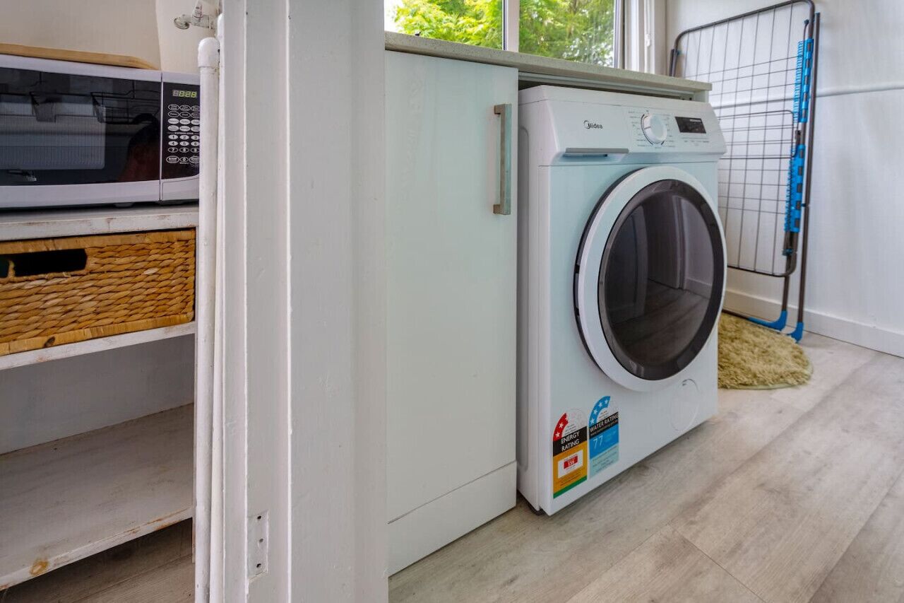 A compact laundry room with a front-loading washing machine, a microwave, and a wicker basket on a shelf.