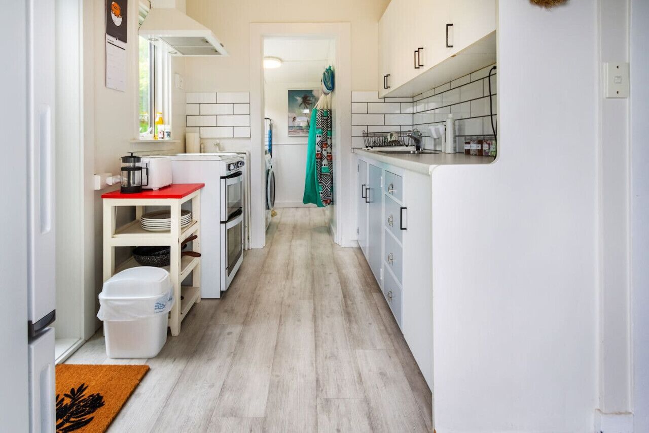 Een smalle keuken met witte kasten, een rode aanrecht en een houten vloer.