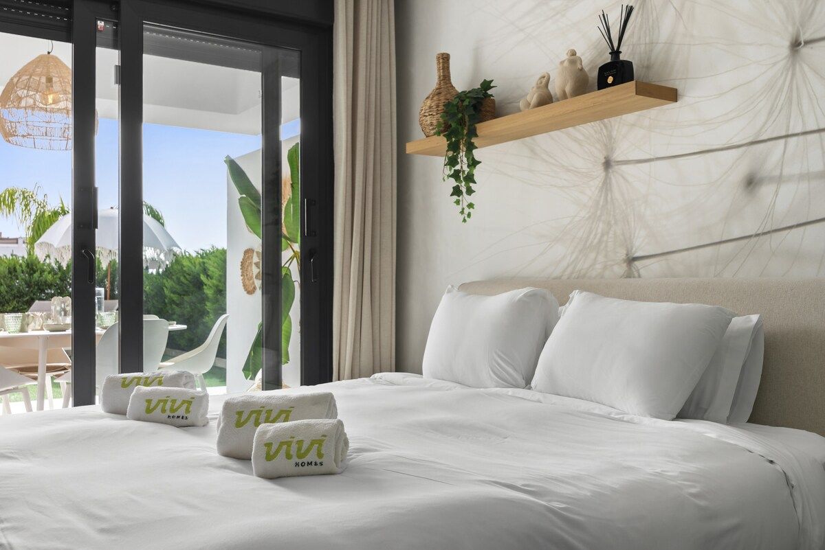 Une chambre d’hôtel avec un lit, des serviettes blanches, une étagère en bois ornée d’objets décoratifs et une vue sur l’extérieur.