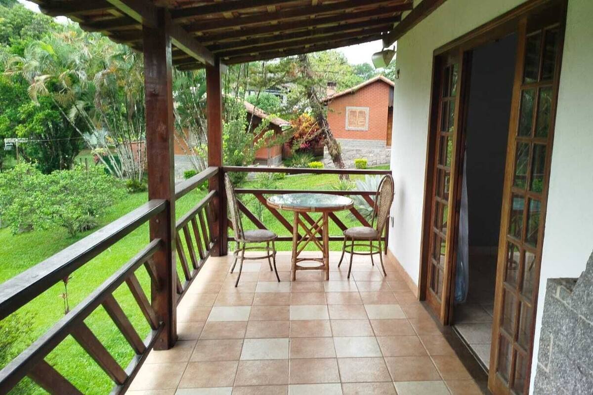 Um alpendre coberto com mesa e cadeiras, uma parede de pedra e vista para um jardim e edifícios ao fundo.