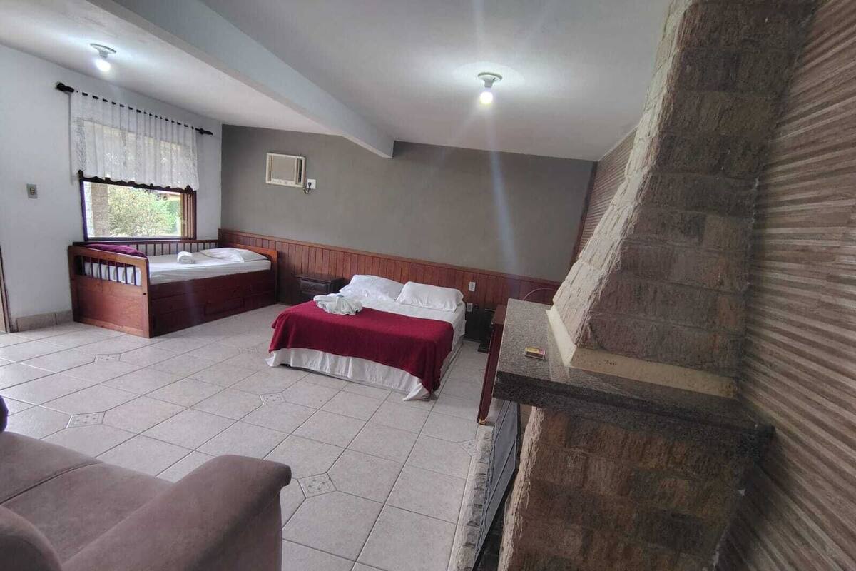 Quarto com duas camas, janela com cortinas, cabeceira de madeira e piso de azulejos.