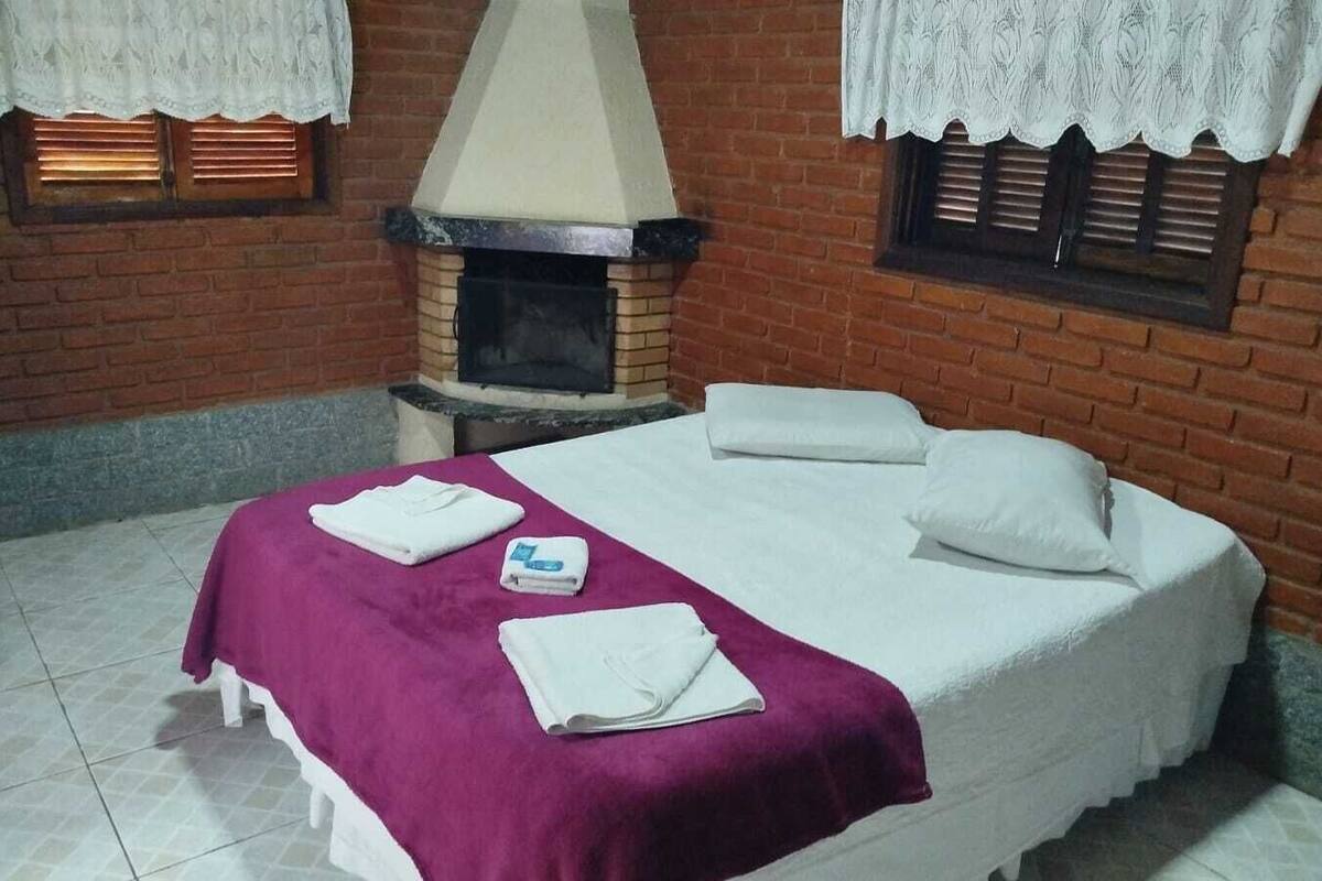 Um quarto com uma cama, lareira e janela com cortinas de renda.