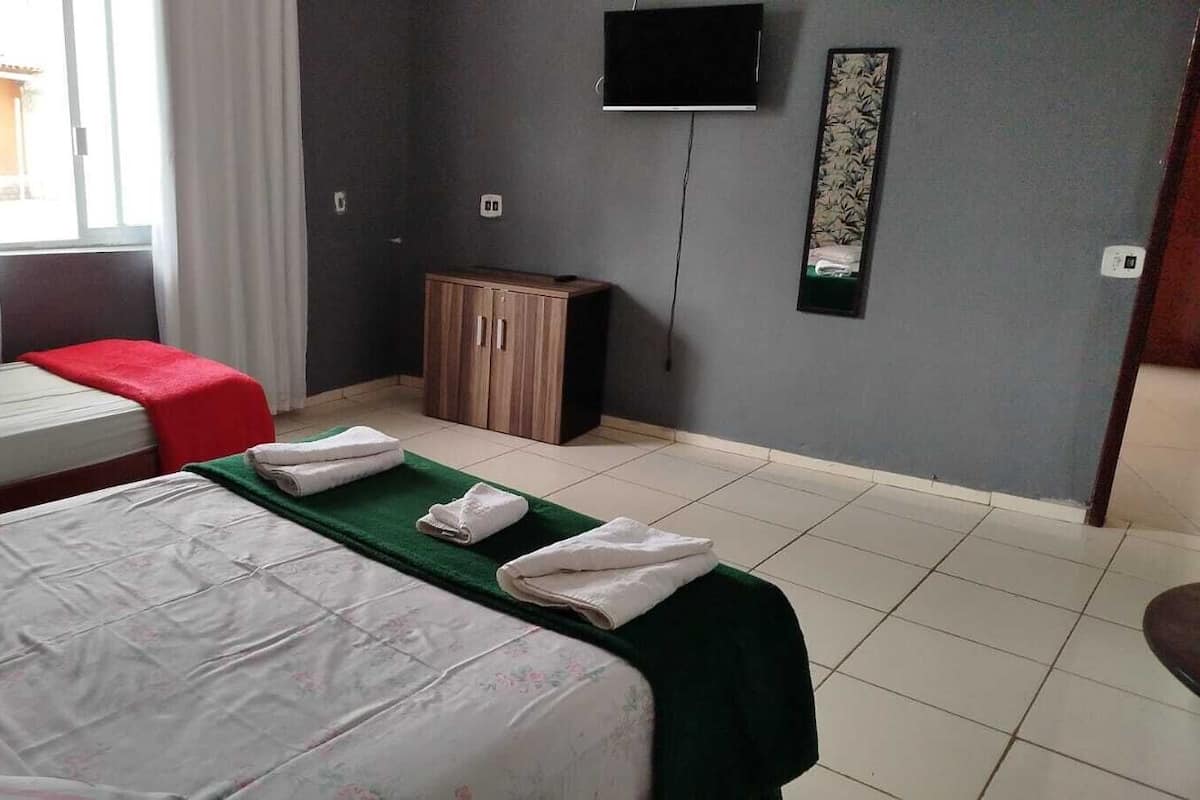 Quarto de hotel com duas camas, televisão, armário e janela com cortinas.