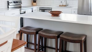 Una cocina moderna con armarios blancos, electrodomésticos de acero inoxidable, una isla grande con taburetes y una mesa de comedor de madera.
