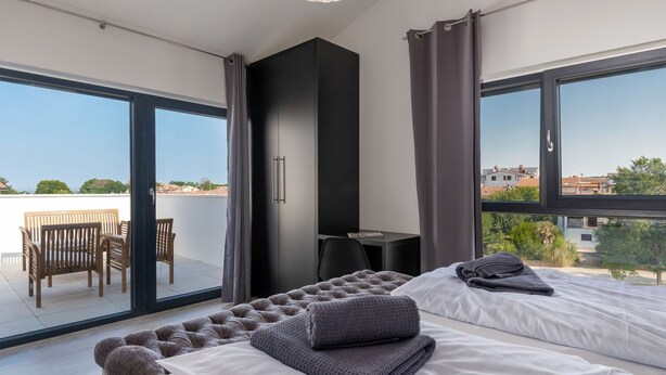 A modern bedroom with a large bed, a small desk, and a balcony with a table and chairs. - Villa Maestral (Istria - Funtana) (Funtana)