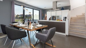 A modern kitchen with a dining area, featuring a glass table, grey chairs, and a view of the outside. - Villa Maestral (Istria - Funtana) (Funtana)