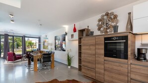 Uma cozinha moderna com forno Bosch, armários de madeira e um espaço de refeições com uma cadeira vermelha e uma mesa de vidro.