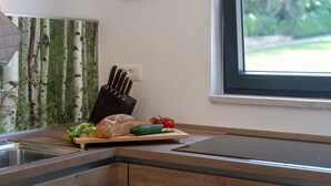 Cozinha com bancada de madeira, tábua de corte com pão e vegetais, porta-facas e janela com vista para vegetação.