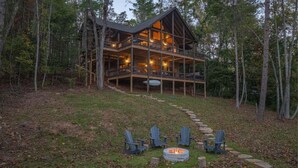 A cabin with a wooden exterior, multiple decks, and a fire pit with chairs in front. - Dialed Inn- Pet Friendly | Dock on Private Lake | Arcade Games (Morganton)