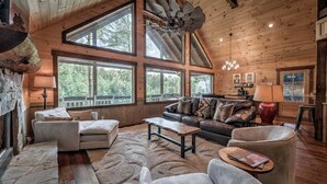 A spacious living room with a large sectional sofa, a coffee table, and a fireplace. There are large windows providing natural light and views of the outdoors. - Dialed Inn- Pet Friendly | Dock on Private Lake | Arcade Games (Morganton)