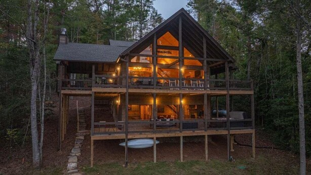 A two-story log cabin with a balcony and a fireplace visible inside. - Dialed Inn- Pet Friendly | Dock on Private Lake | Arcade Games (Morganton)