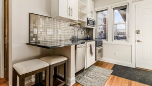 A compact kitchen with white cabinetry, a tiled backsplash, a microwave, and a window with a view of buildings.