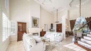 A spacious living room with a fireplace, white sofas, a chandelier, and a staircase leading to another level.