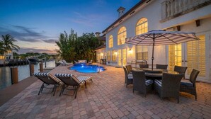 A pool area with lounge chairs and a table, surrounded by a brick patio.