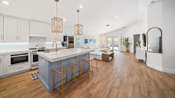A modern kitchen with white cabinets, a large island with bar stools, and pendant lighting. - 246 Managed by Brampton Park (Delray Beach)