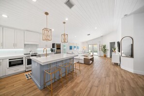 Une cuisine moderne avec des meubles blancs, un grand îlot central doté de tabourets et un éclairage suspendu.