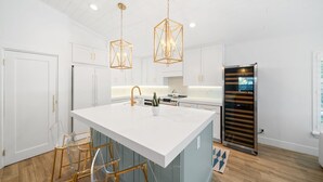 A modern kitchen with a central island, white cabinetry, gold fixtures, and a built-in oven. - 246 Managed by Brampton Park (Delray Beach)