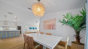 A modern kitchen with white cabinetry, a central island, and a dining area with a white table and wicker chairs. - 246 Managed by Brampton Park (Delray Beach)