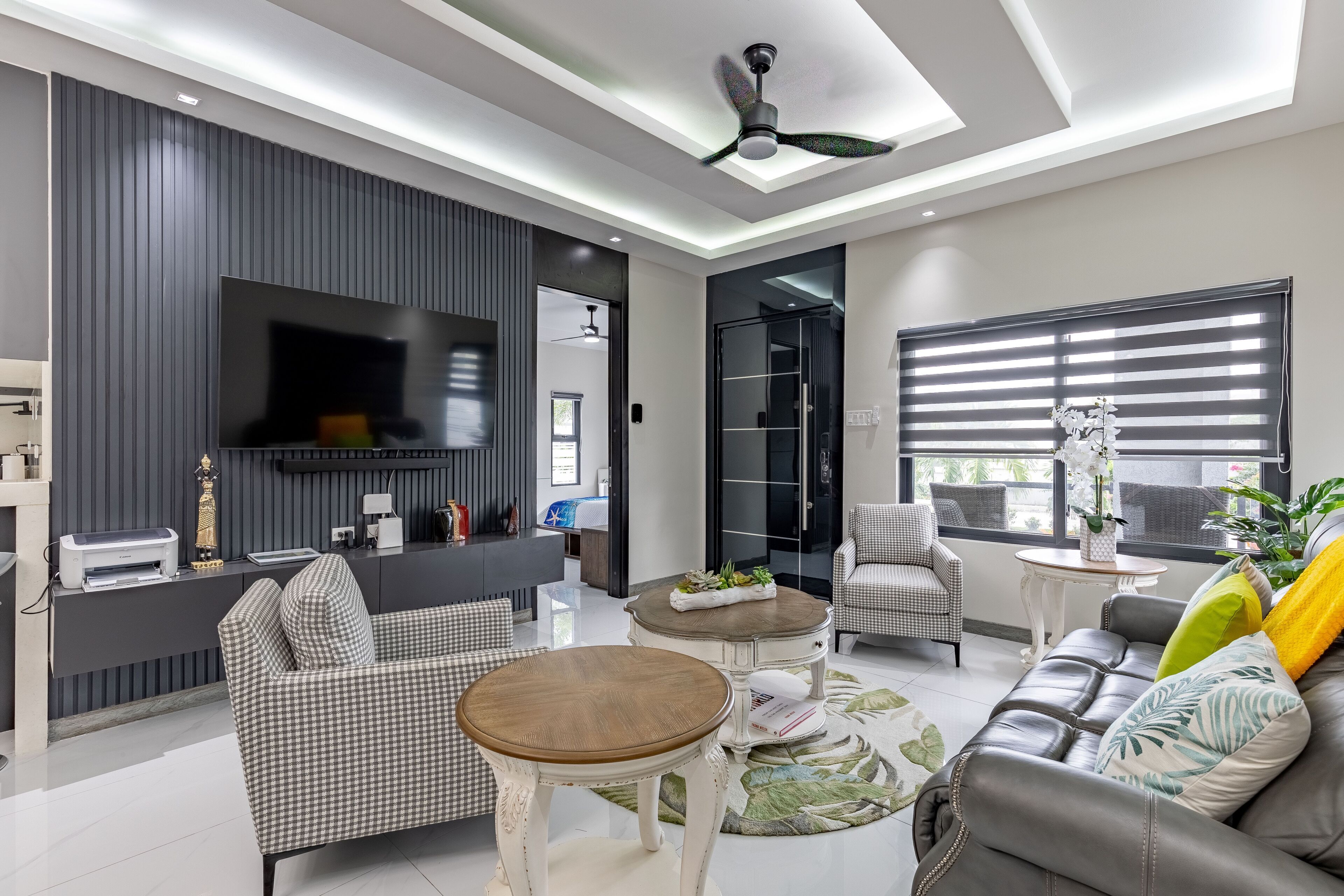 A modern living room with a flat-screen TV, a ceiling fan, and a sofa with decorative pillows.
