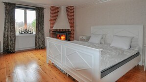 A bedroom with a brick fireplace, a large bed with white bedding, and a window with curtains. - Gorgeous home in Vretstorp (Vretstorp)