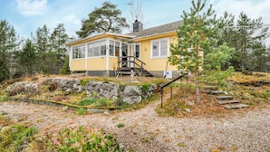 A yellow cabin with a covered porch and a chimney, surrounded by trees and rocky terrain. - Gorgeous home in Vretstorp (Vretstorp)