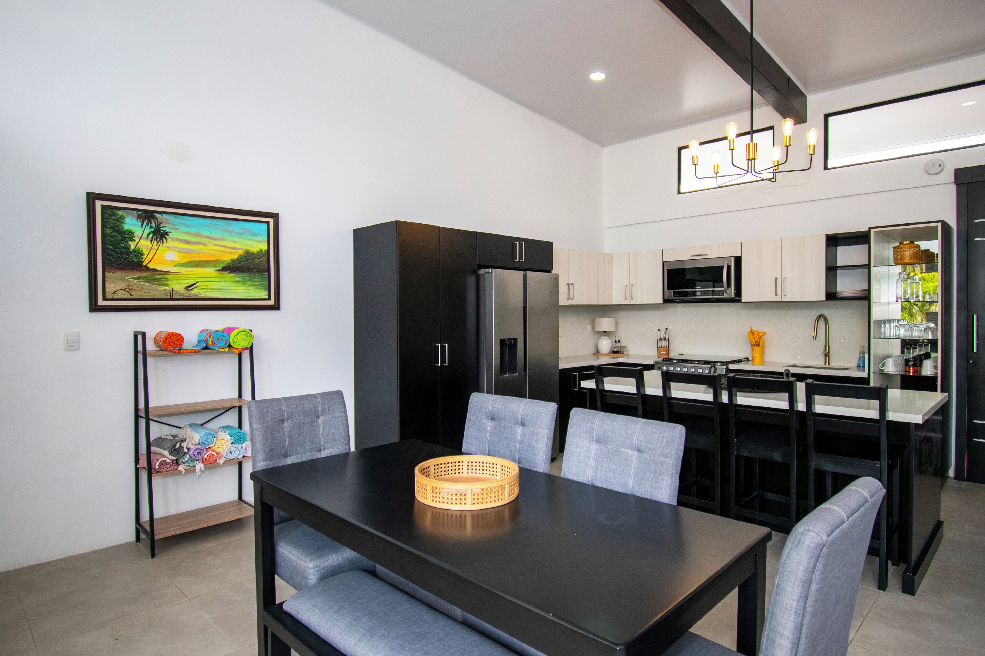 A modern kitchen with a dining area, featuring a black refrigerator, microwave, and a chandelier.