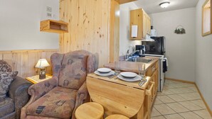 Une cuisine compacte avec des meubles en bois, une table à manger avec de l’assiette et des couverts, et un petit réfrigérateur.