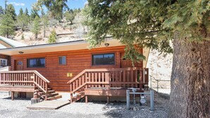 Une cabane en bois avec une terrasse, un escalier et un grand arbre devant.