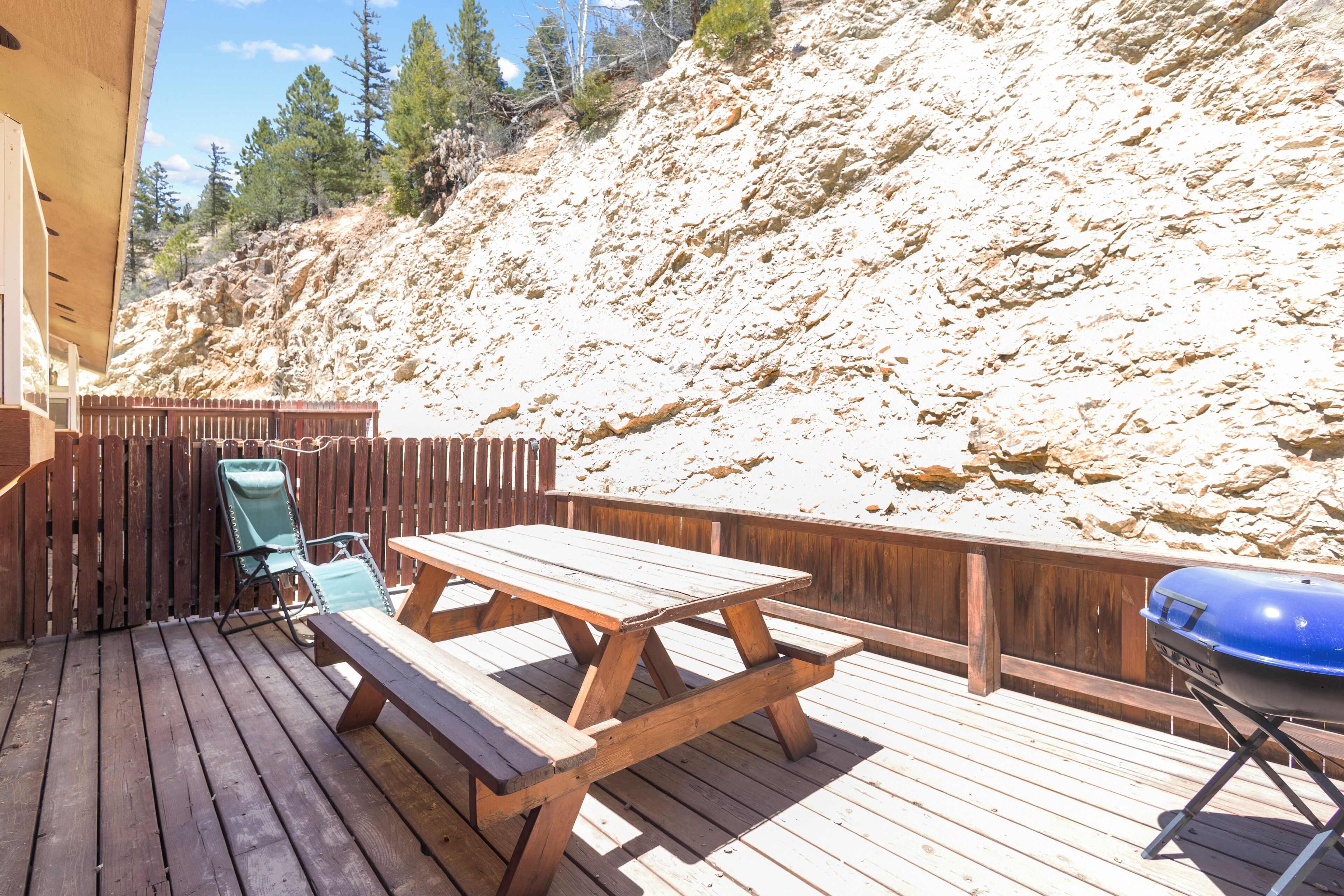 A wooden deck with picnic tables and a barbecue grill.