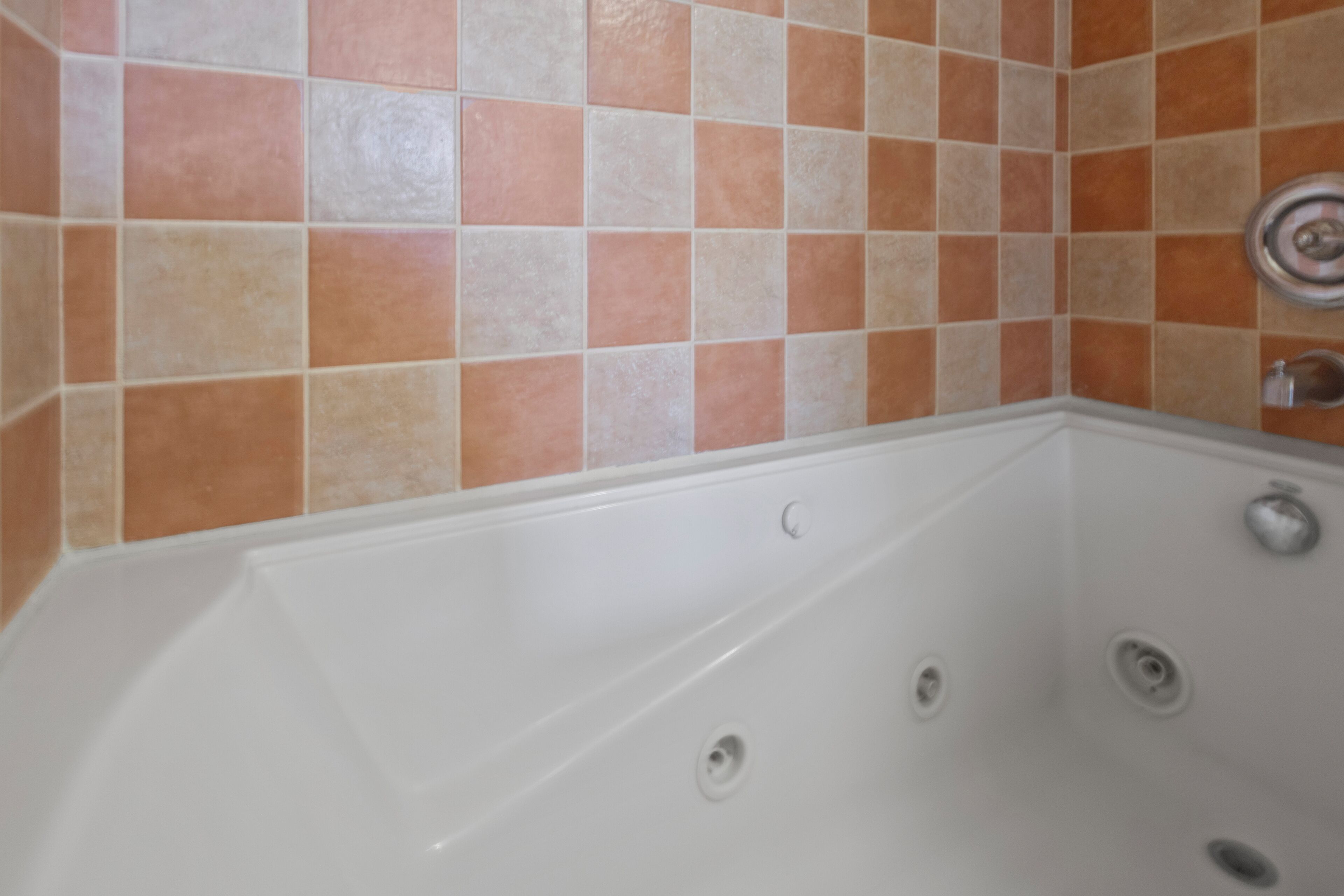 A bathtub with a white interior, set against a wall with orange and beige tiles.