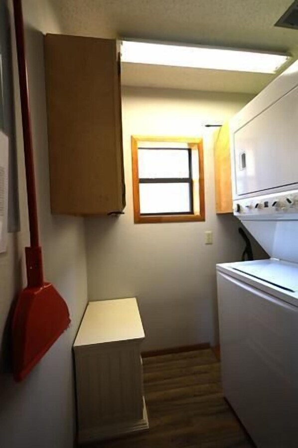 A small kitchen with a refrigerator, a window, and a red broom.