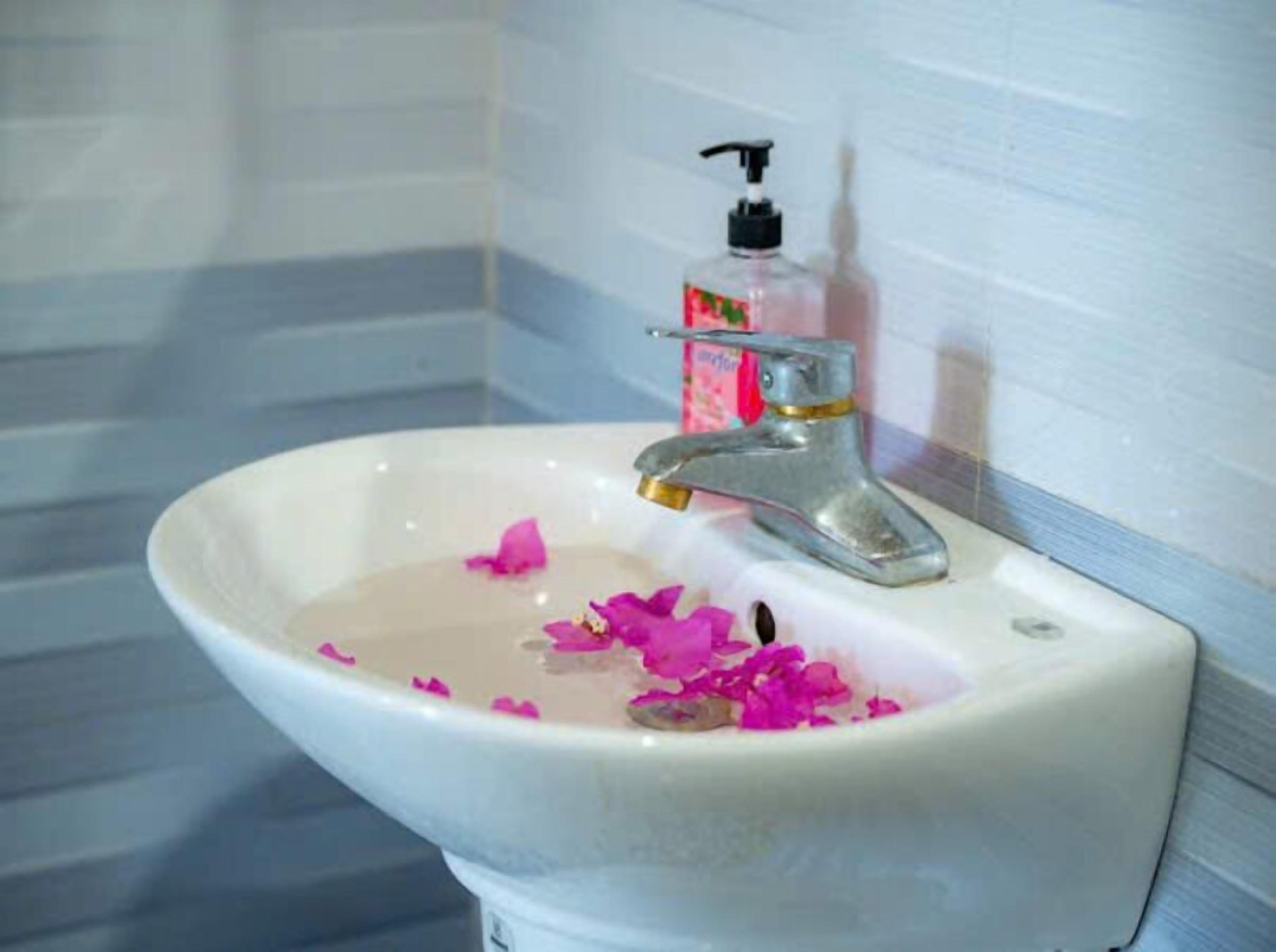 Un lavamanos con grifo, dispensador de jabón y pétalos de flores rosados en el agua.