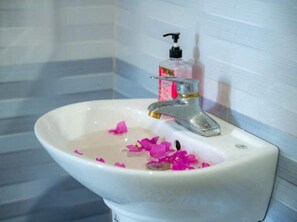 Un lavamanos con grifo, dispensador de jabón y pétalos de flores rosados en el agua.