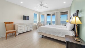 A bedroom with a bed, a chair, a dresser, a television, and a balcony with a view.