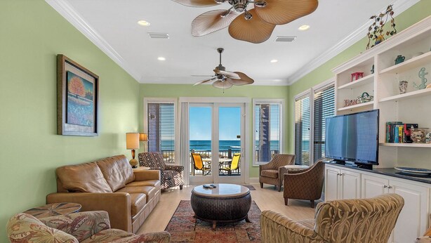 A spacious living room with a view of the ocean, a ceiling fan, and a television on a cabinet.