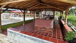 A covered outdoor area with a bamboo roof, red and grey tiled floor, and brick walls.