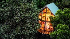 A cabin with a wooden deck and a balcony, surrounded by dense forest. - Cozy Getaway From It All ~ Heated Pool ~ Sauna ~ Hot Tub ~ Games ~ A-Frame (Sevierville)