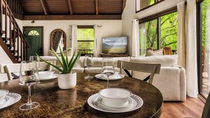 A dining area with a wooden table set for four, surrounded by a cozy living space with a sofa and a television. - Cozy Getaway From It All ~ Heated Pool ~ Sauna ~ Hot Tub ~ Games ~ A-Frame (Sevierville)