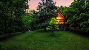 A wooden cabin with a glass facade, surrounded by lush greenery and a well-maintained lawn. - Cozy Getaway From It All ~ Heated Pool ~ Sauna ~ Hot Tub ~ Games ~ A-Frame (Sevierville)