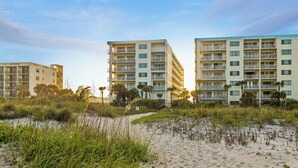 A beachfront hotel with multiple floors, balconies, and a sandy beach in the foreground. - Charming Sandcastles Condo – Steps to the Beach w/ Pool, Hot Tub & Tennis! (Cocoa Beach)