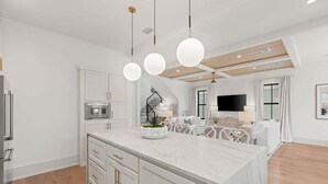 Een moderne keuken met een groot eiland, witte kastjes en hanglampen.