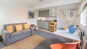 A compact living space with a sofa, a small table, a kitchen area, and a dining table. - 2 Lion Cottages, Knodishall (Knodishall)