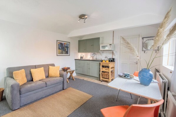 Un espacio habitable compacto con sofá, pequeña mesa, zona de cocina y mesa de comedor.