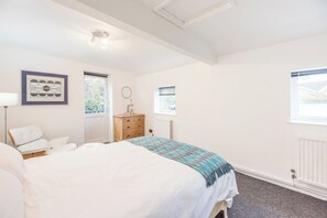 Un dormitorio con una cama, un aparador, una silla y dos ventanas.