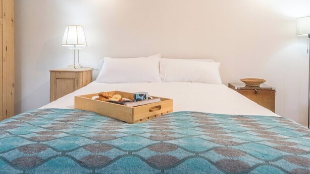 A neatly made bed with a blue patterned bedspread, a wooden bedside table with a lamp, and a tray of breakfast items on the bed. - 2 Lion Cottages, Knodishall (Knodishall)