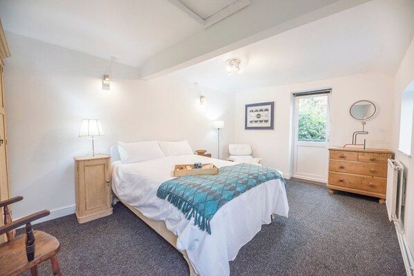Un dormitorio con cama, mesitas de noche, cómoda, silla y ventana.