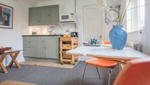 A compact kitchen with green cabinets, a microwave, and a small dining area with a table and chairs. - 2 Lion Cottages, Knodishall (Knodishall)
